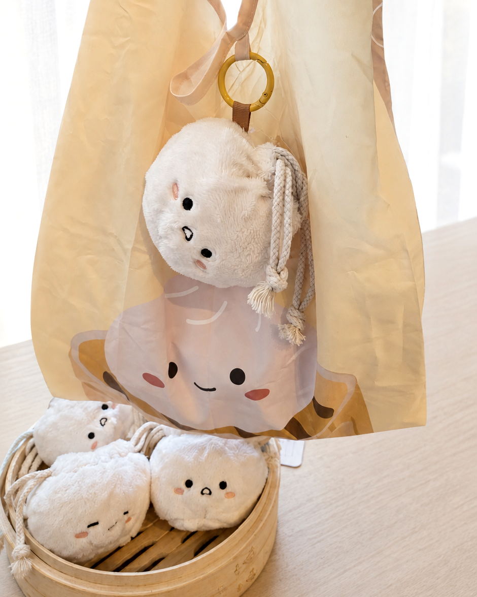 A beige tote bag with a mesh pocket holding several small plush character pouches, alongside a bamboo tray holding more matching plush pouches on a light wood table.
